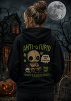 Person wearing a black hoodie with a chibi voodoo doll anti‑stupid design in a spooky gothic Halloween scene with pumpkins and moon
