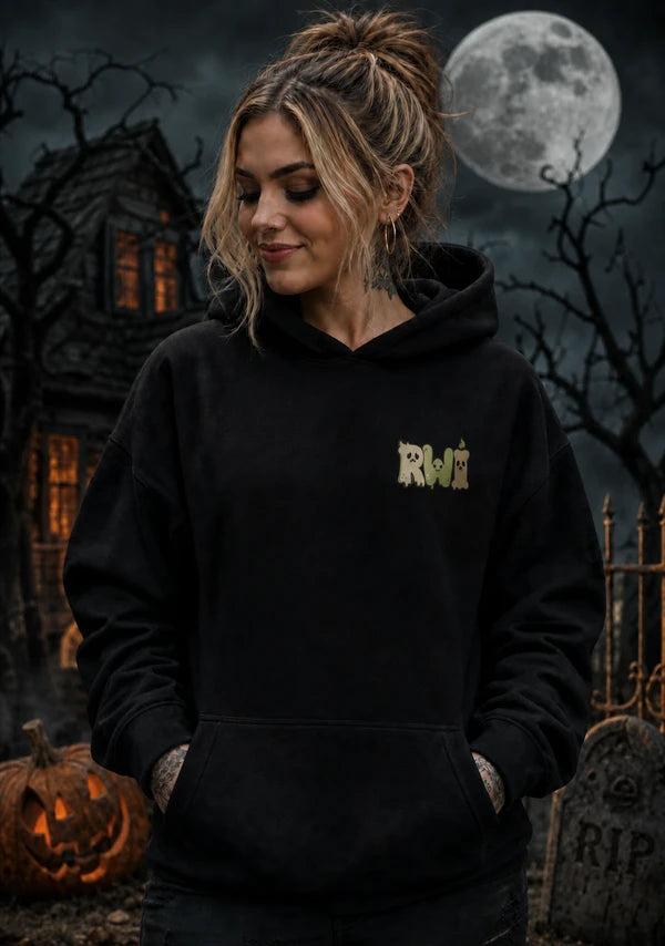 Person wearing a black RWI hoodie in a spooky Halloween scene with a gothic house, full moon, jack‑o’-lantern and gravestone