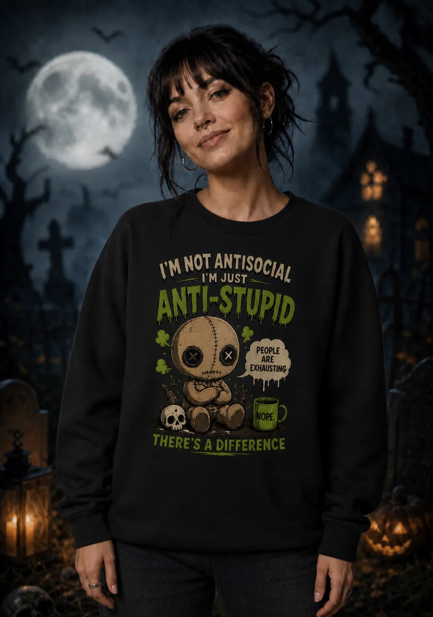 Woman in dark sweatshirt with chibi voodoo doll design and text “I’m not antisocial, I’m just anti‑stupid.”