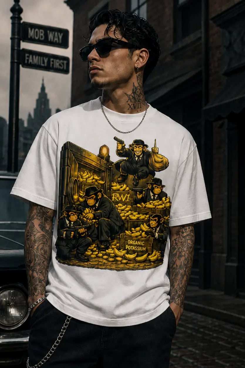 A person wearing a treasure‑heist cartoon tee stands on a wet cobblestone street with a vintage car, brick buildings and noir night atmosphere.