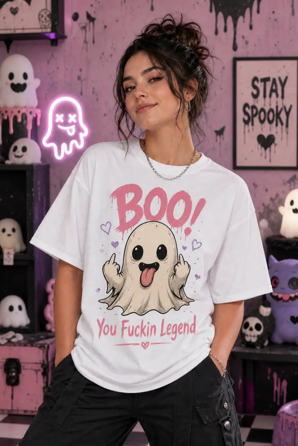 Person wearing a white T‑shirt with a playful ghost design and bold humorous text, standing in a pastel spooky Halloween room
