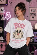 Person wearing a white T‑shirt with a playful ghost design and bold humorous text, standing in a pastel spooky Halloween room