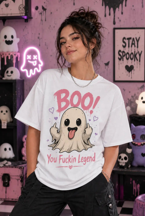 Person wearing a white T‑shirt with a playful ghost design and bold humorous text, standing in a pastel spooky Halloween room