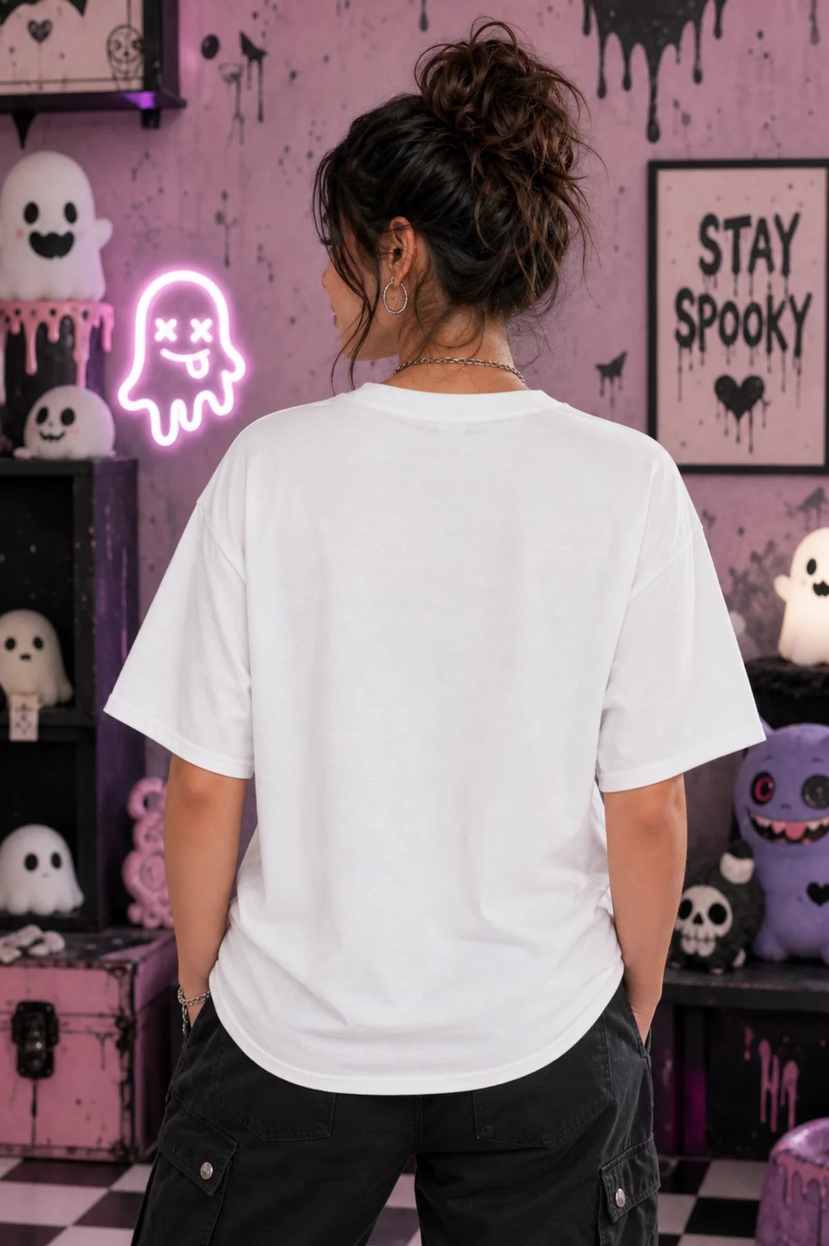 Person facing away in a pastel spooky room wearing an oversized white T‑shirt, surrounded by cute ghost décor and neon ghost light