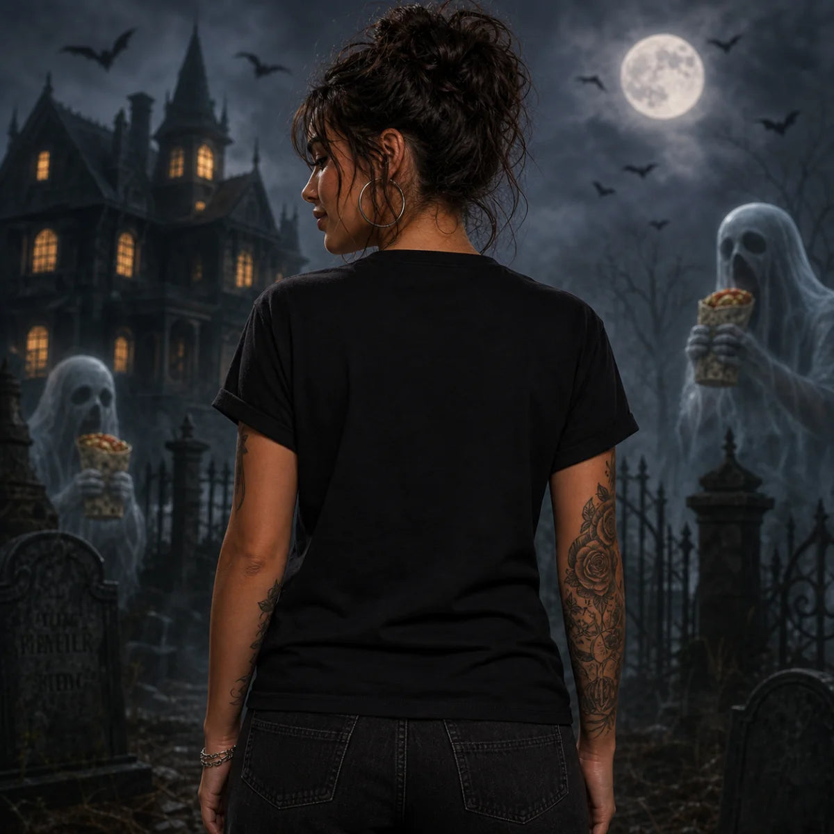 Tattooed woman seen from behind wearing a black t‑shirt in a spooky graveyard with haunted house, tombstones, and full moon.