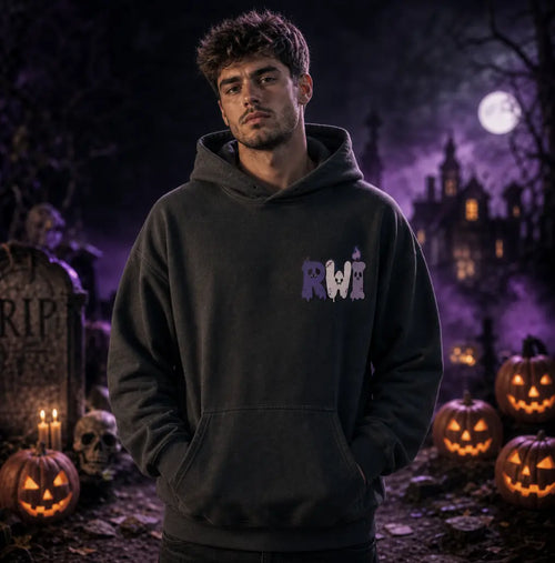 Person in Halloween graveyard scene wearing black hoodie with dripping RWI design, standing amid pumpkins, tombstones and purple mist