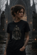 Woman in black hooded‑figure graphic T‑shirt standing amid gothic statues and cathedral archway with small glowing candles