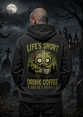 A man stands in a moonlit graveyard wearing a dark hoodie with a zombie graphic and the text “Life’s Short Drink Coffee