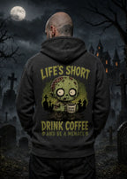 A man stands in a moonlit graveyard wearing a dark hoodie with a zombie graphic and the text “Life’s Short Drink Coffee