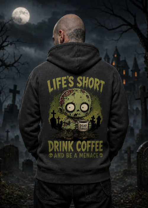 A man stands in a moonlit graveyard wearing a dark hoodie with a zombie graphic and the text “Life’s Short Drink Coffee