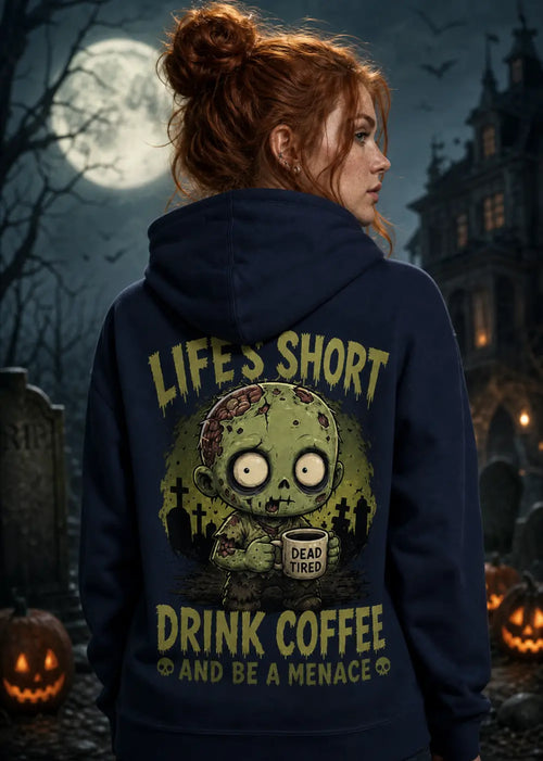 A woman stands in a moonlit graveyard wearing a navy hoodie with a zombie graphic and “Life’s Short Drink Coffee.”