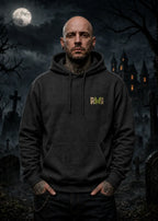 A man stands in a moonlit graveyard wearing a dark hoodie with a small green‑gold “RWI” logo on the chest