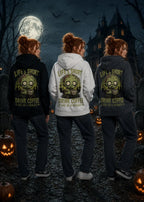 Three women stand in a moonlit graveyard wearing hoodies with zombie graphics and “Life’s Short Drink Coffee” text.