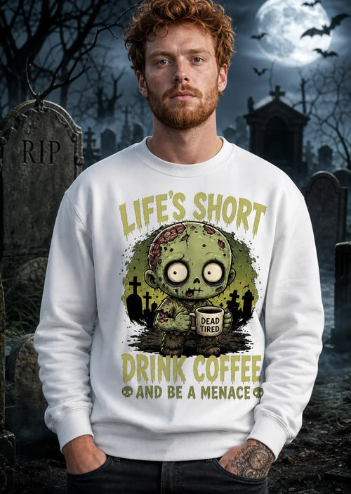 A man stands in a moonlit graveyard wearing a white sweatshirt with a zombie graphic and “Life’s Short Drink Coffee” text.