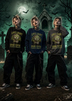 Three women stand in a green‑lit graveyard wearing black, navy, and gray sweatshirts with zombie graphics and coffee text.