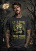 A man stands in a moonlit graveyard wearing a dark T‑shirt with a zombie graphic and “Life’s Short Drink Coffee” text.