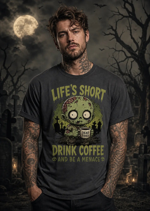 A man stands in a moonlit graveyard wearing a dark T‑shirt with a zombie graphic and “Life’s Short Drink Coffee” text.