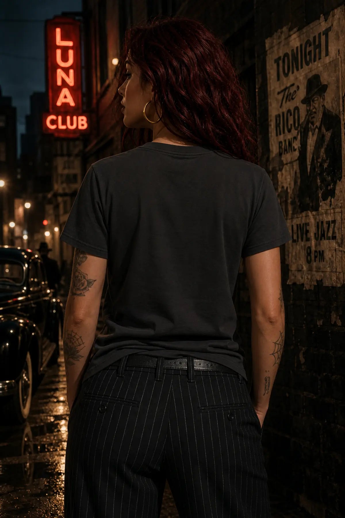 A person with dark red hair stands with their back to the camera in a wet night street wearing a dark gray T‑shirt and pinstripe trousers.