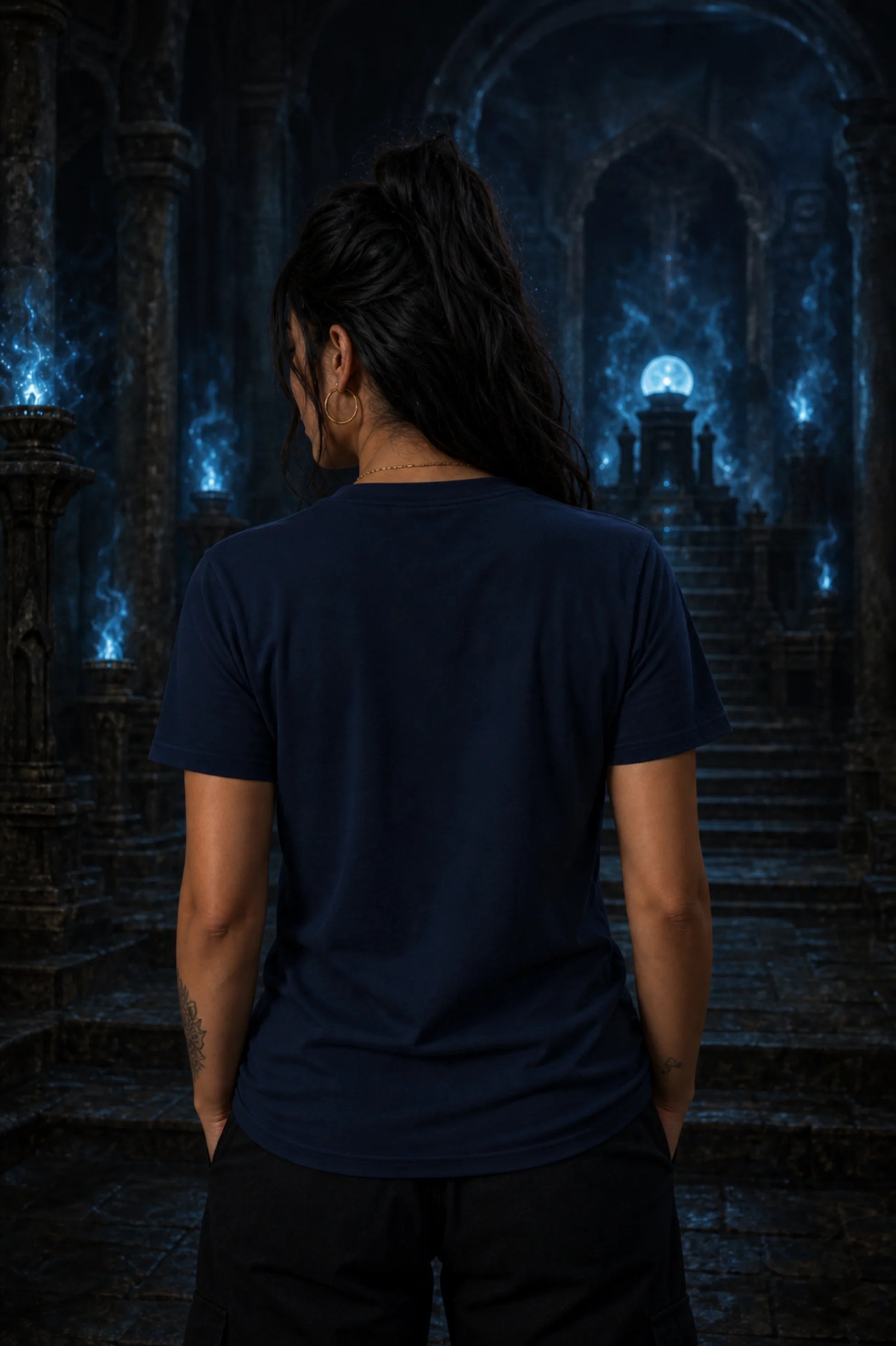Woman with long dark hair in a navy tee standing with her back to a blue‑lit ancient stone hall filled with glowing flames and columns