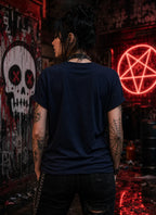 Person facing away in dark punk outfit with tattoos and chains, standing in neon‑lit graffiti scene featuring skull art and red symbol