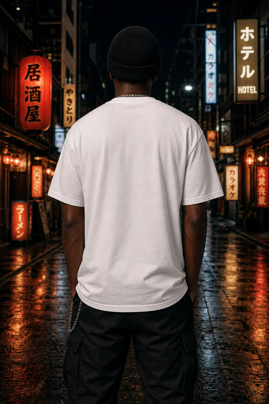 A man seen from behind in a white T‑shirt, black cargo pants and a beanie on a wet neon‑lit Japanese street at night.