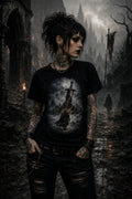 Tattooed person in ripped black jeans and a sword‑art tee standing in misty gothic ruins with spires rising behind them