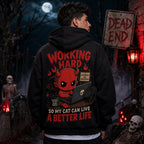 Person wearing a black hoodie with a red devil cat‑lover design in a spooky graveyard scene with skeletons, tombstones and red light
