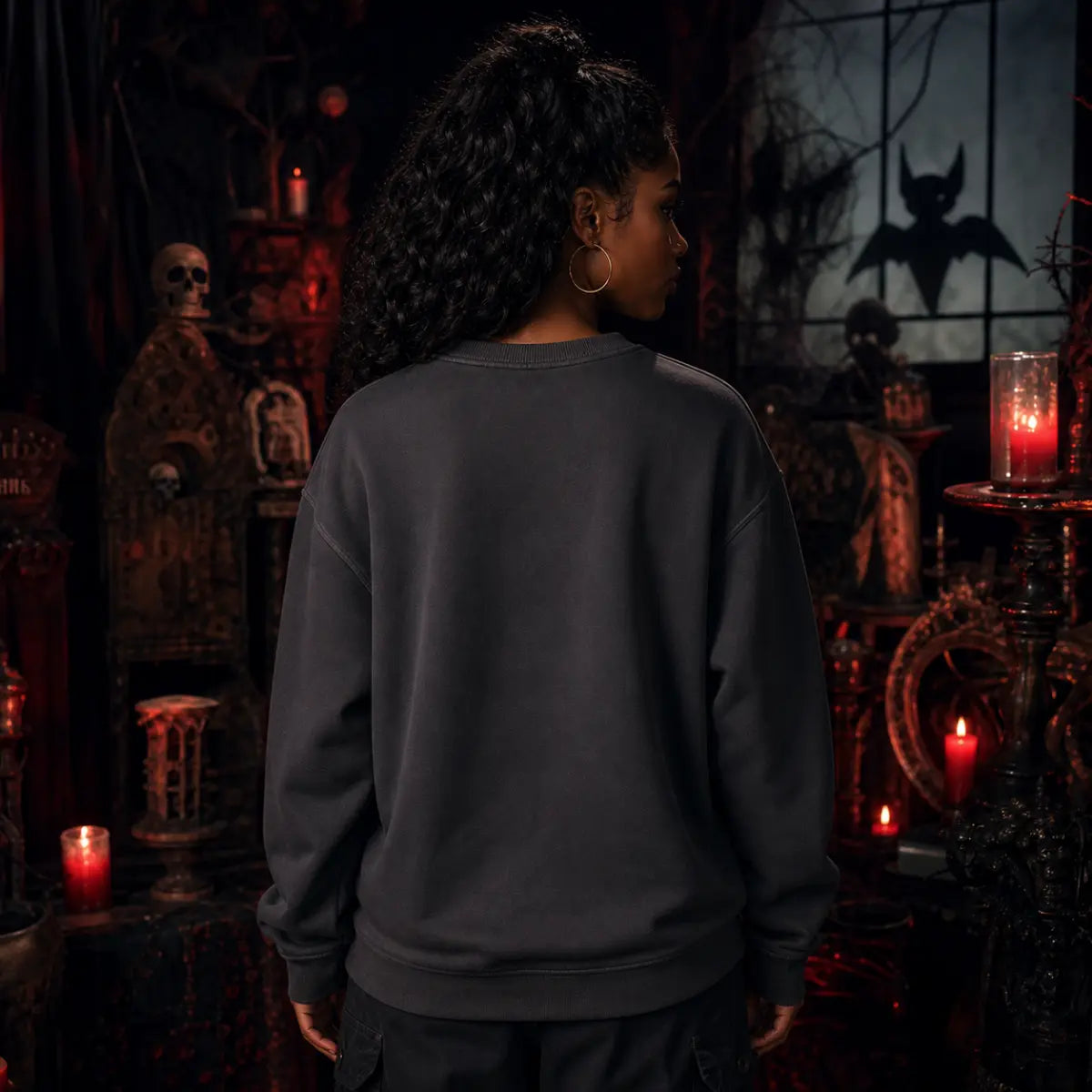 Person facing away in a gothic room with red candles, skull décor and dark furniture while wearing a plain dark sweatshirt