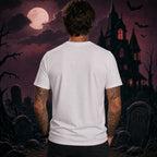Person facing away wearing a plain white T‑shirt in a spooky Halloween scene with a haunted house, full moon, bats and gravestones